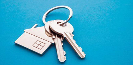 2 keys in a keychain with a small house placed on a blue surface