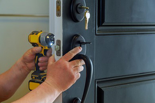 Gray door with a key on the keyhole and someone drilling the lock with a yellow driller