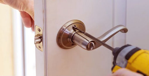 An electric drill screwing in a lock to a white door